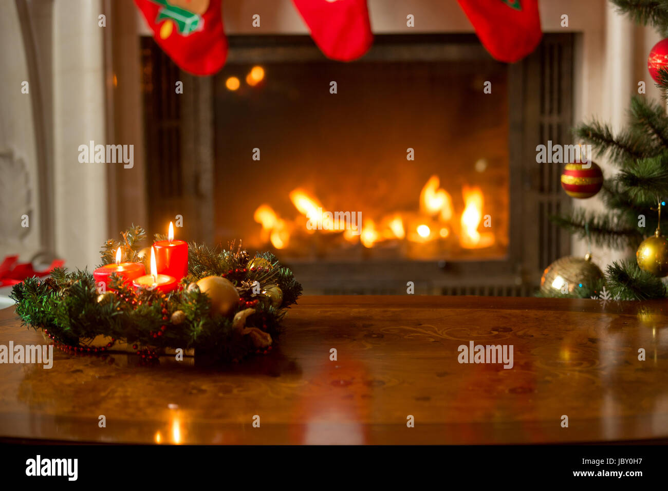 Beautiful Christmas background with burning candles on wooden table in front of fireplace and Christmas tree Stock Photo