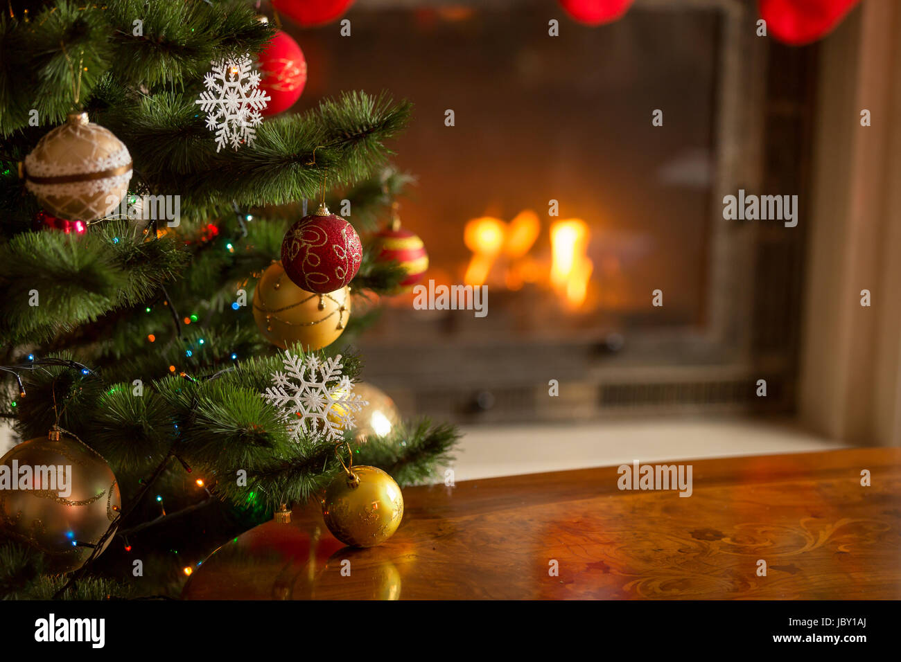 Closeup image of golden and red baubles on Christmas tree in front of burning fireplace. Beautiful Christmas background Stock Photo