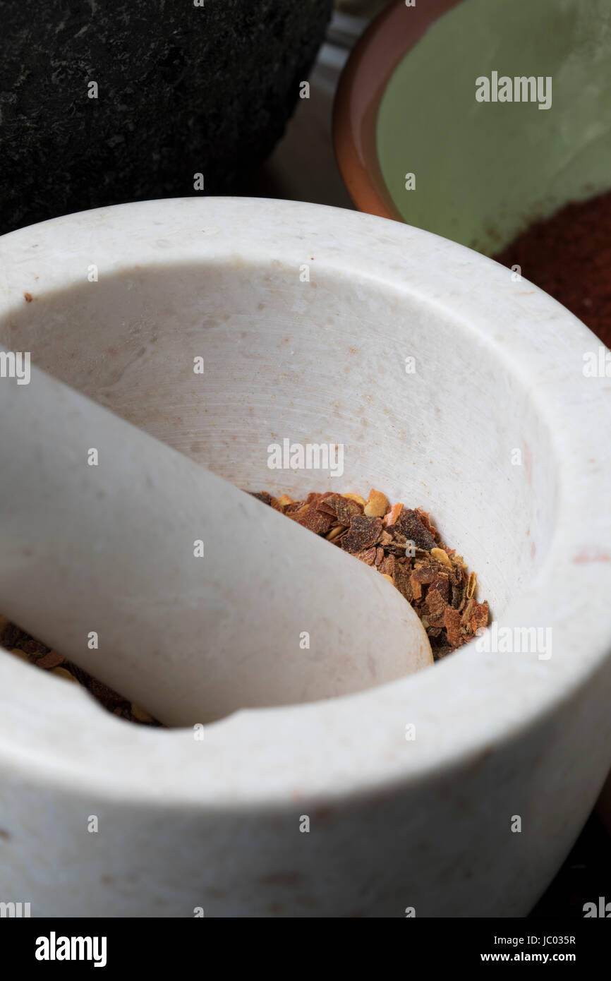 Vertical orientation close up of porcelain mortar and pestle with crushed dried chili pepper. Stock Photo