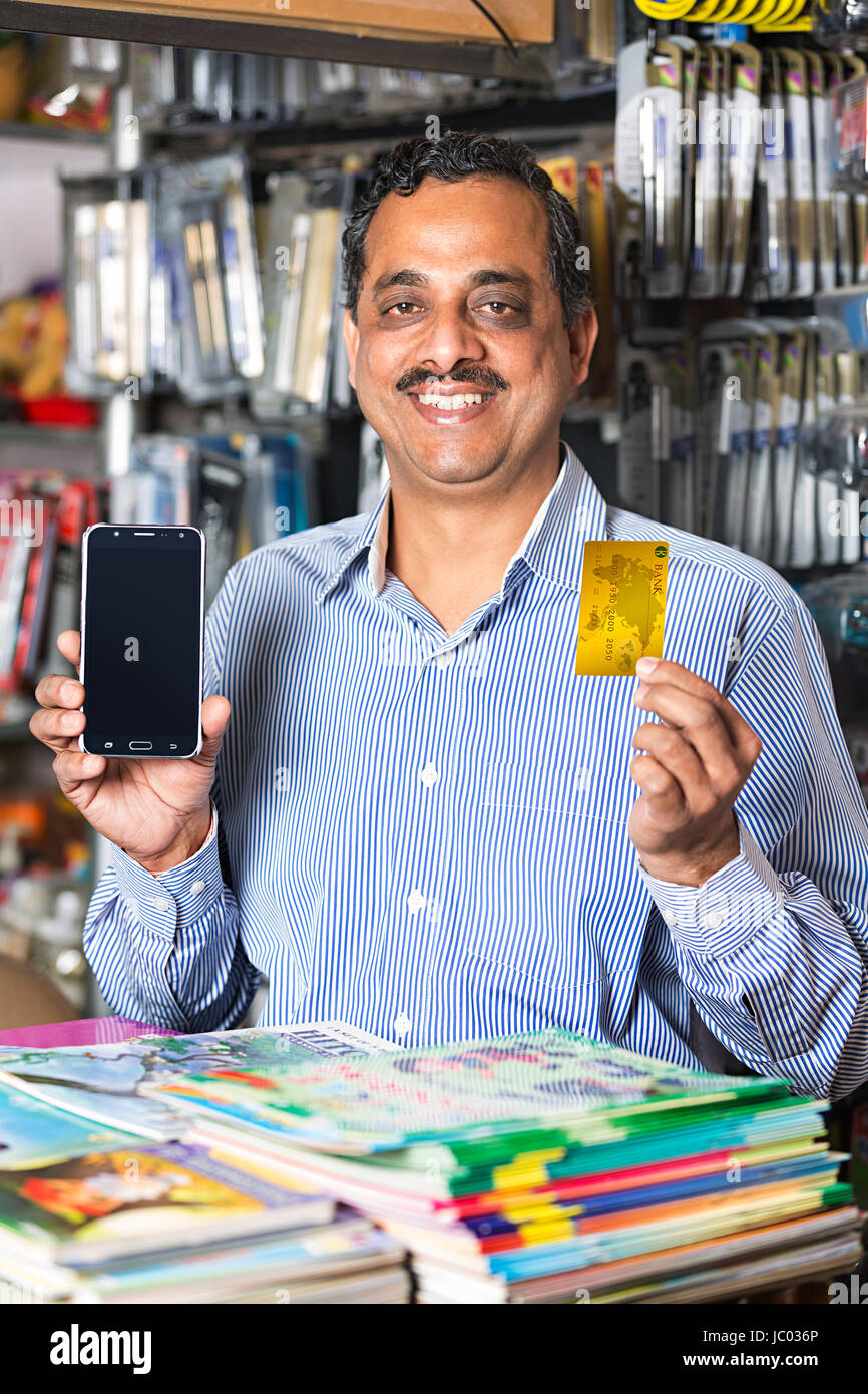 1 Indian Shop Keeper Man Showing Credit Card And Mobile Phone In Stationary Shop Stock Photo