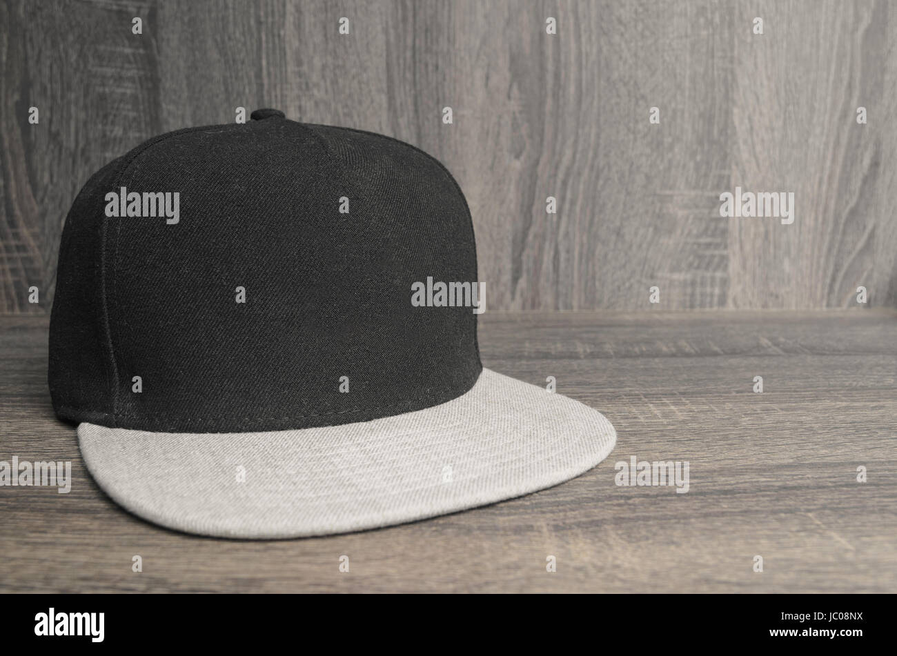 Black cap with light gray flap on a wooden background. Straight flap caps with no brand. Space for text to the side. Stock Photo