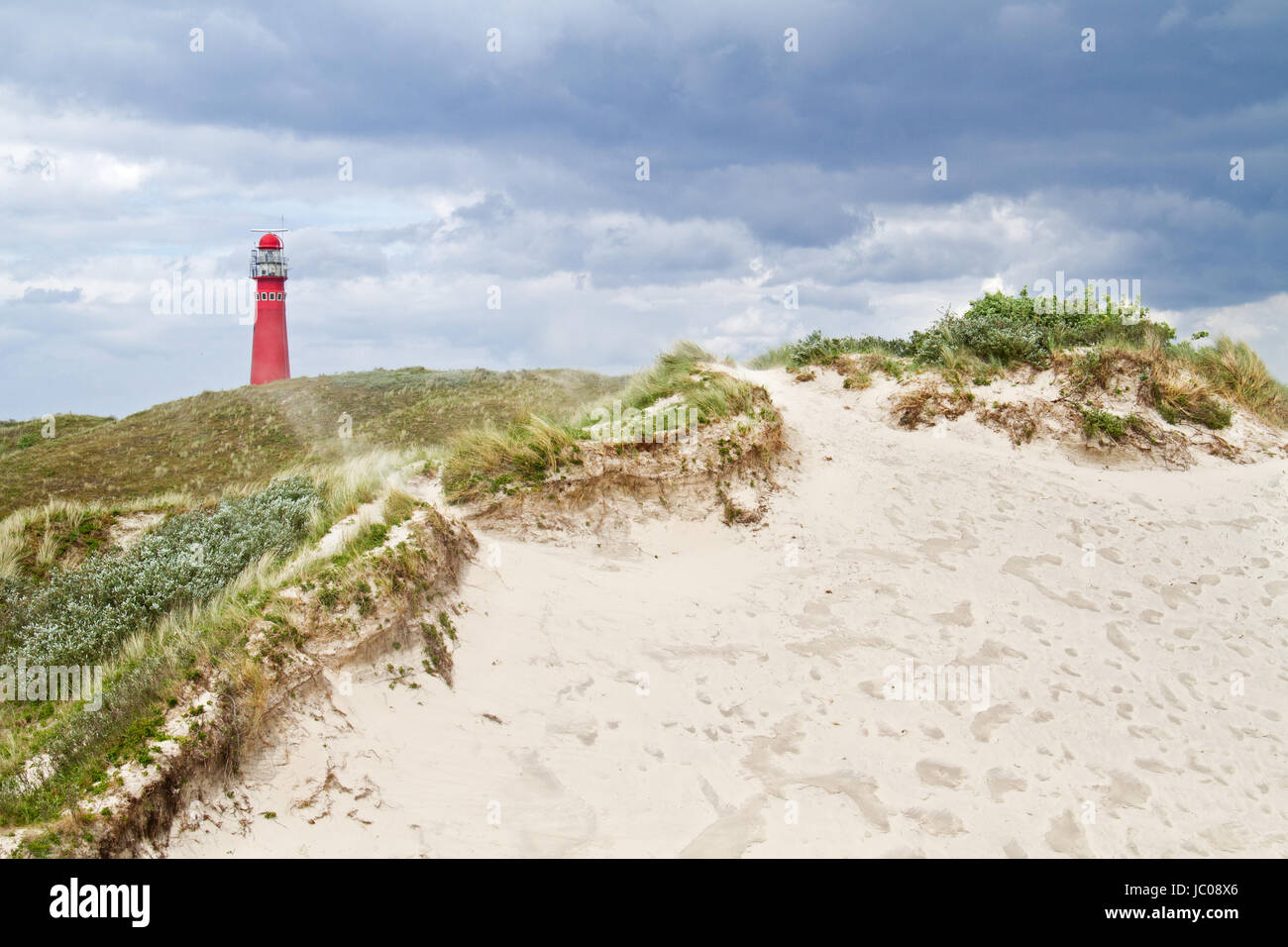 Red lighthouse in the dunes on a windy day, sand blowing in the air Stock Photo
