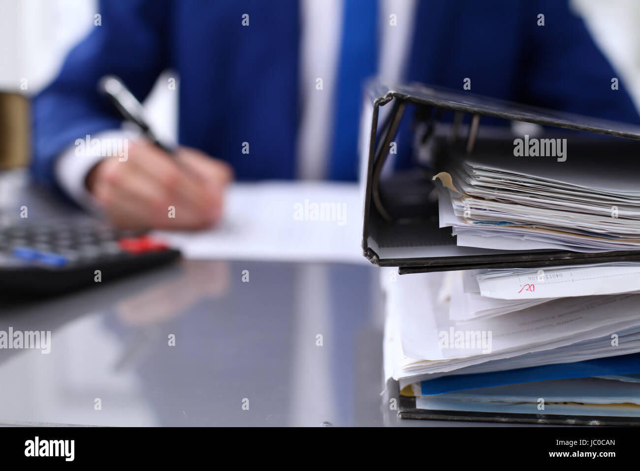 Binders with papers are waiting to be processed with businessman back
