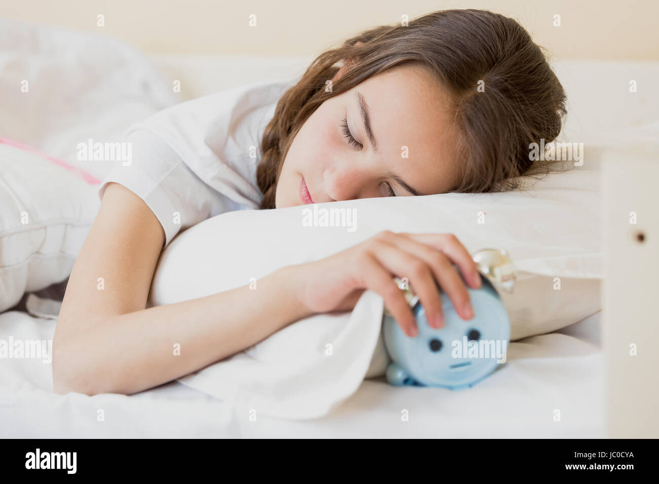 Portrait of cute teenage girl holding alarm clock under pillow Stock