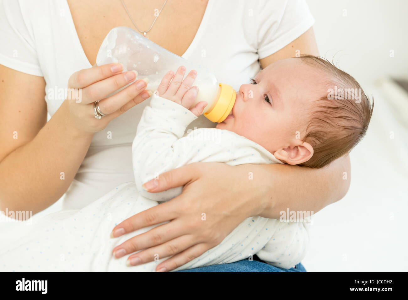 Portrait of mother giving milk from bottle to her baby sleeping on