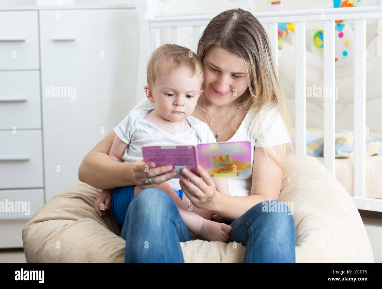 Portrait of beautiful young mother holding baby on her lap and reading