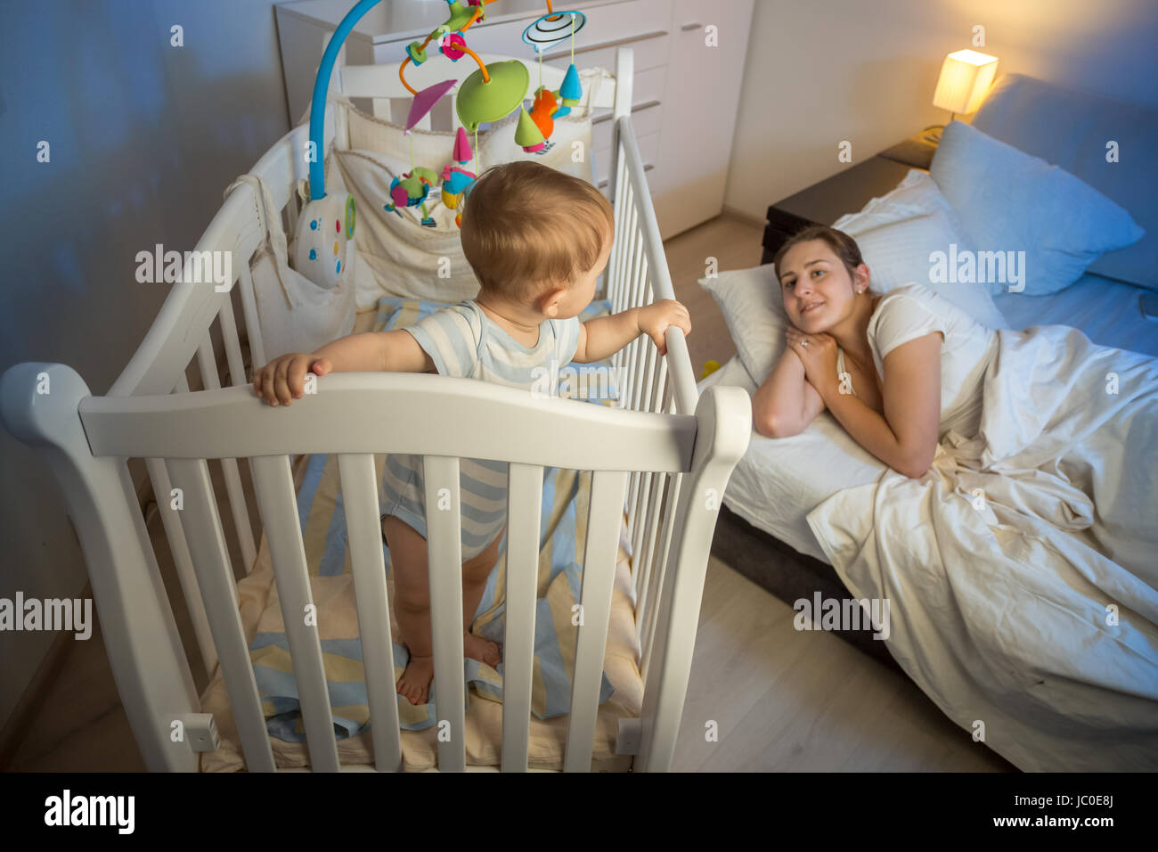 9 months old baby boy standing in crib and waking up his tired mother