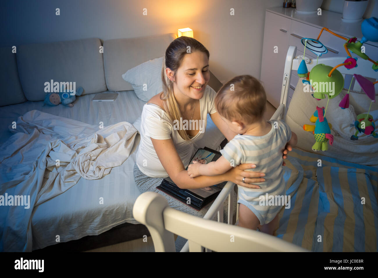 Portrait of beautiful young mother taking baby out of crib at night