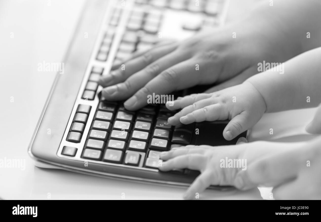 Black and white conceptual shot of adult and baby hands on computer keyboard Stock Photo