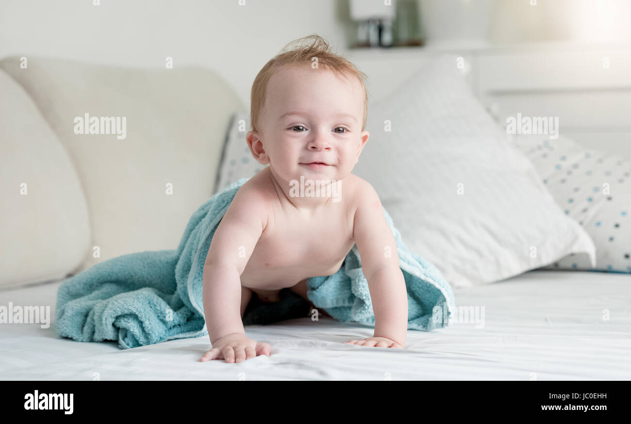 Beautiful 9 months old baby in blue towel after shower crawling on bed