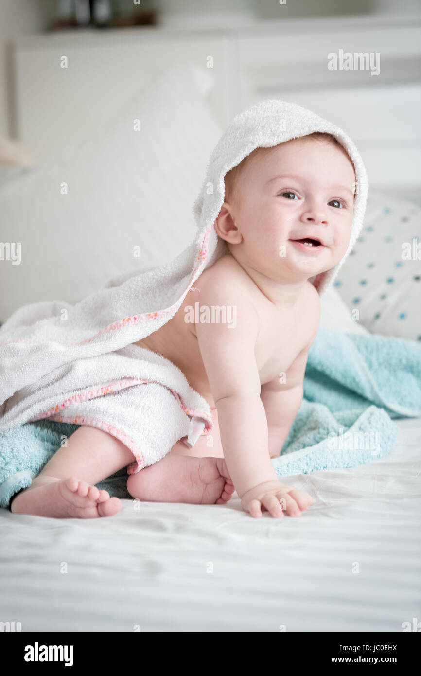 Beautiful smiling 9 months old baby boy sitting on bed covered in towel