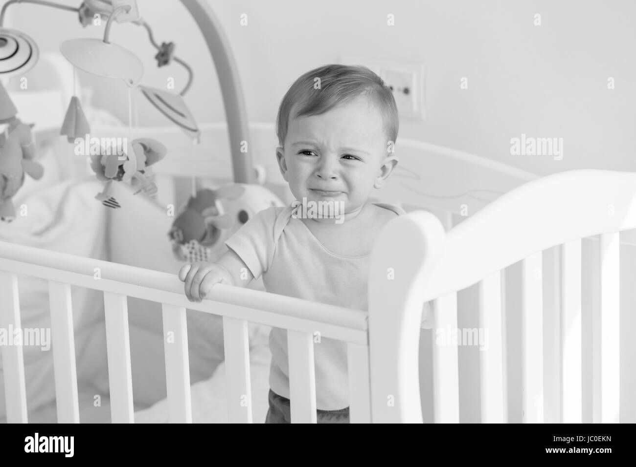 Black and white portrait of baby boy standing in crib and crying Stock Photo