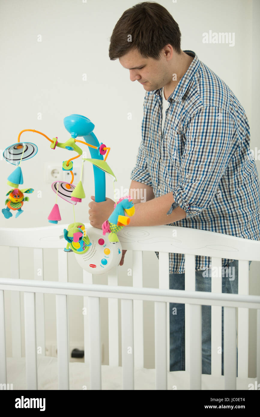 Young caring father assembling baby's cot and putting toy carousel in