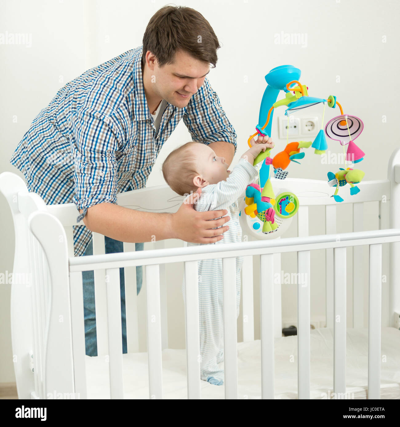 Portrait of young father holding his 9 months old baby son in cot Stock