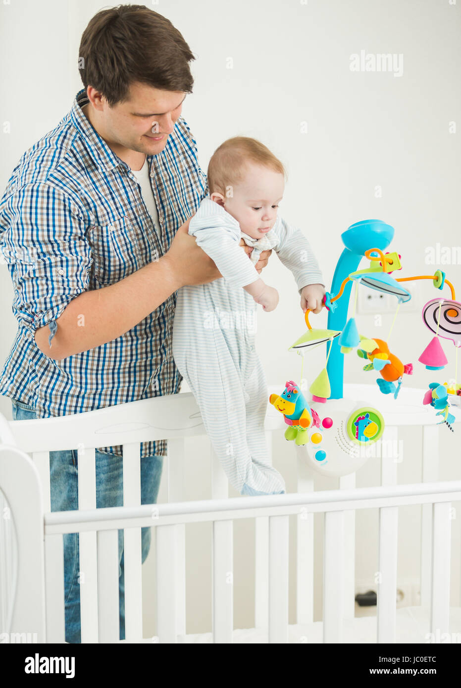 Portrait of young man taking his 9 months old baby son out of cot Stock