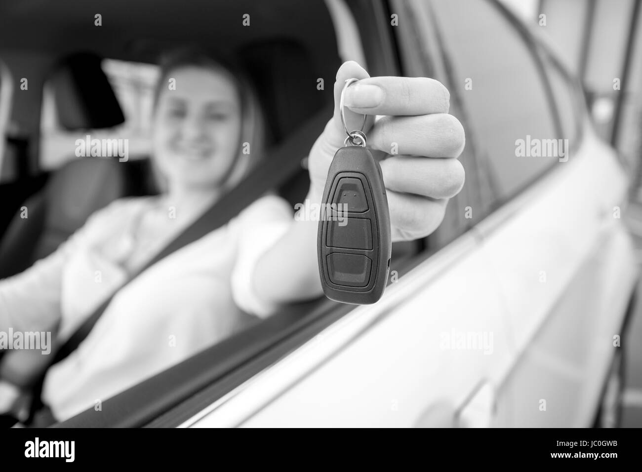 Black and white photo of happy woman showing car keys through open window Stock Photo