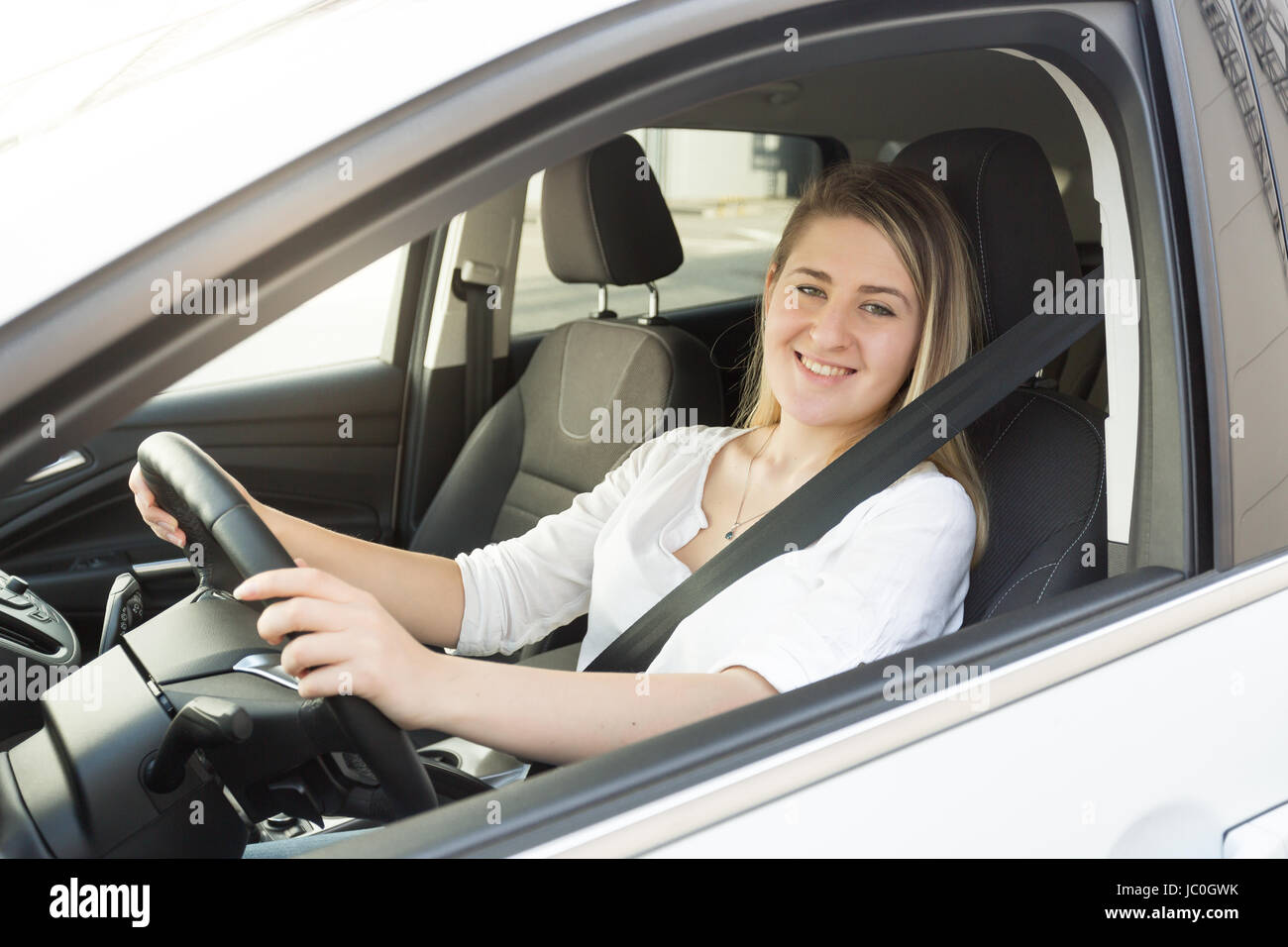 Portrait of smiling blonde woman in white shirt driving car Stock Photo ...