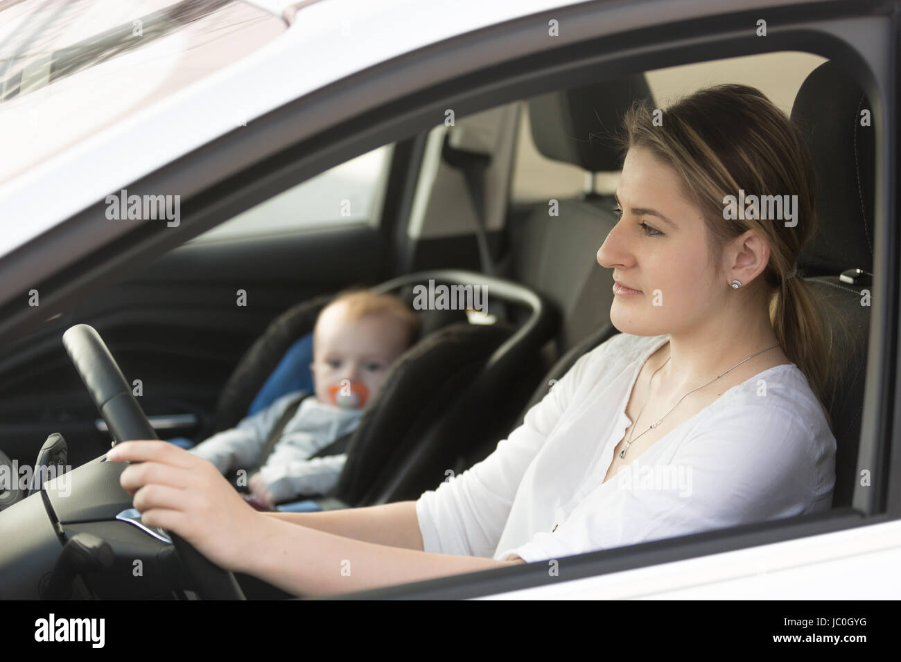Portrait of mother driving car with her baby sitting on front seat Stock Photo