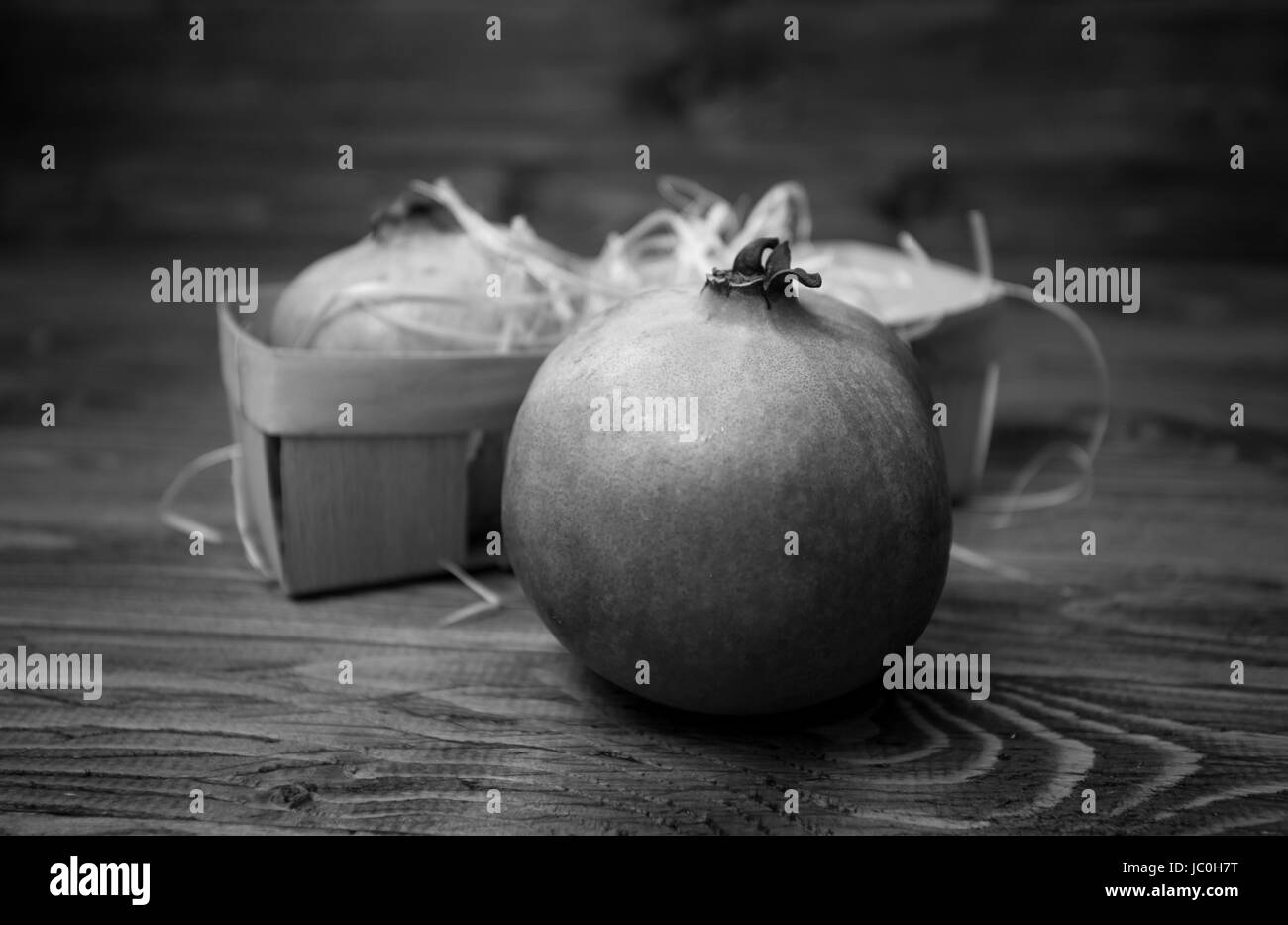 Closeup black and white photo of whole pomegranate lying on old wooden desk Stock Photo