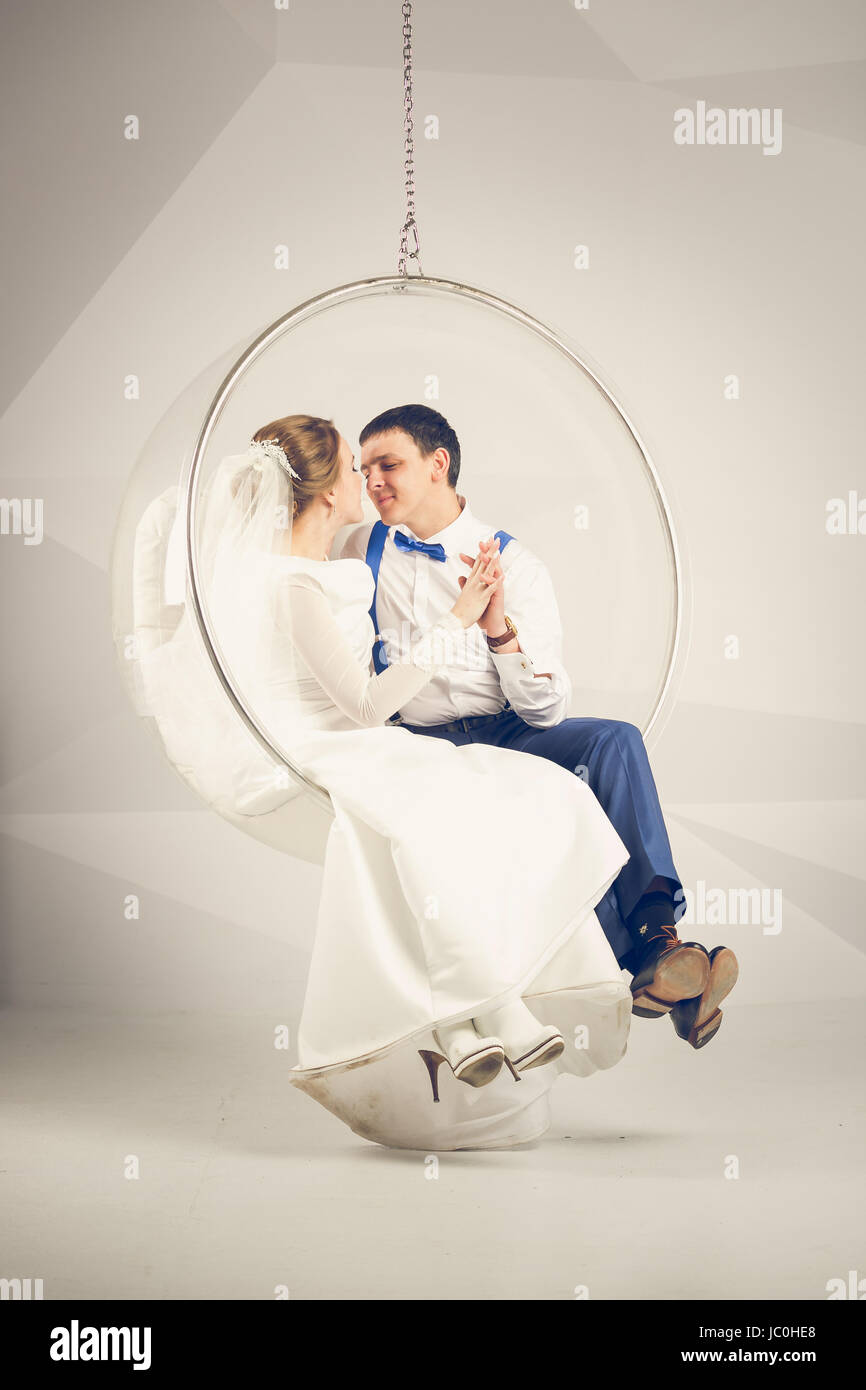 Toned photo of happy bride and groom sitting in plastic swing chair at ...