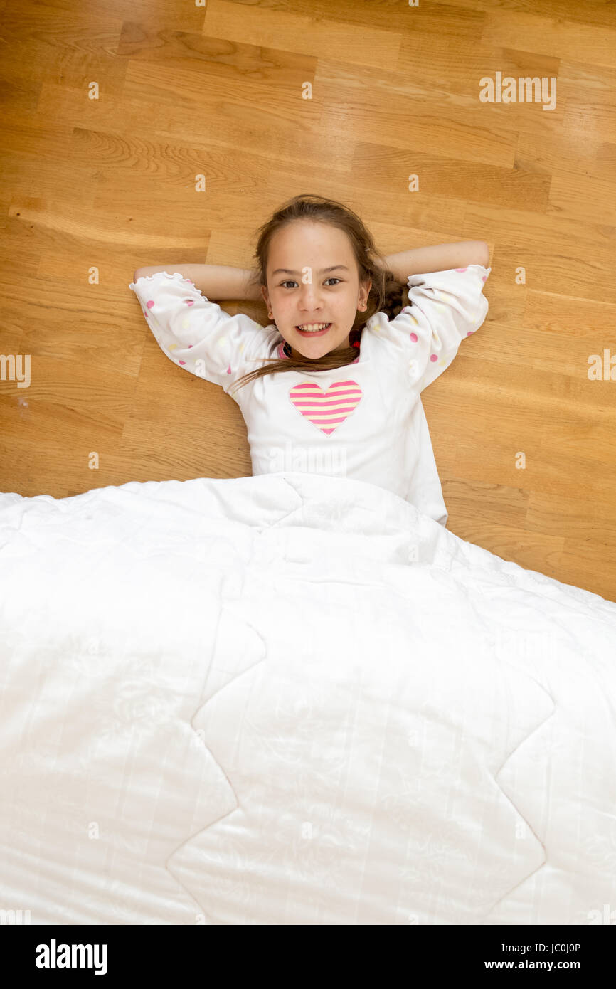 Little smiling girl covered with blanket lying on wooden floor Stock