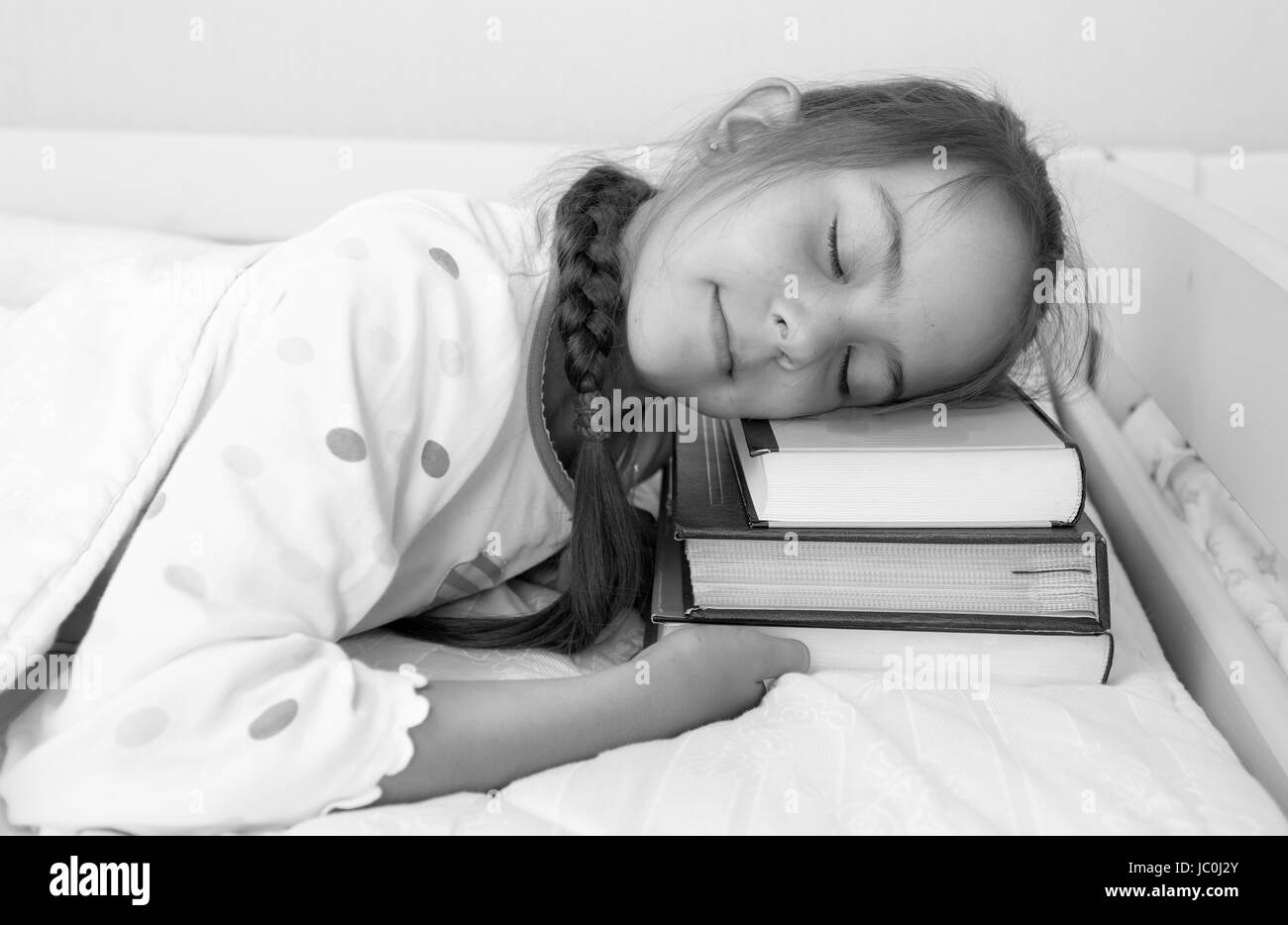 Black and white portrait of little girl sleeping on pile of books at bed Stock Photo