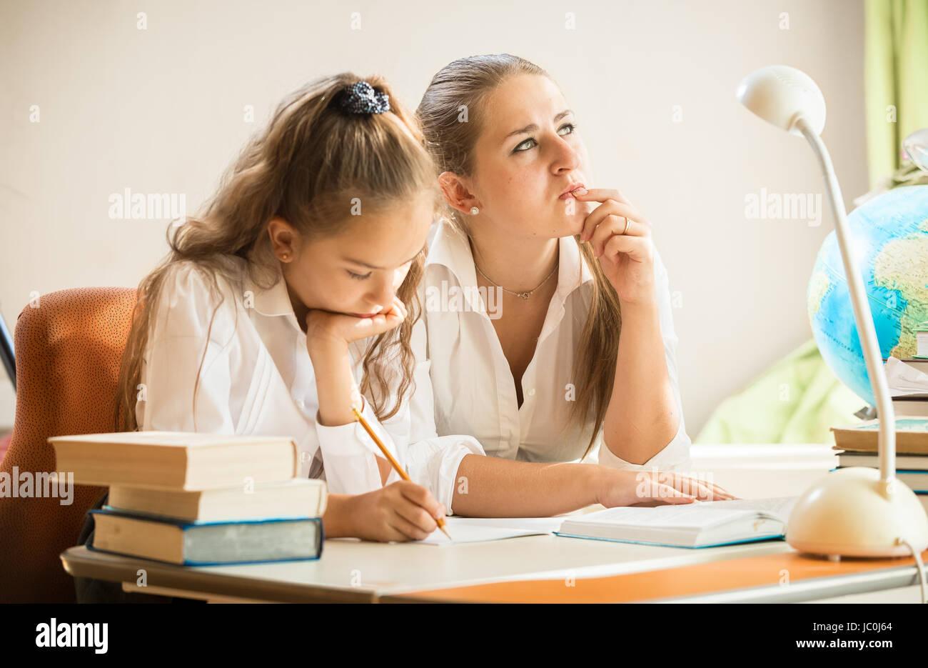 Young mother trying to solve complicated exercise with little daughter Stock Photo