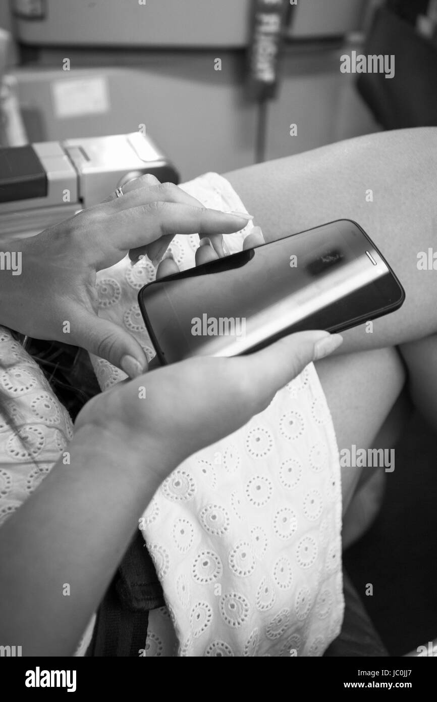 Black and white shot of woman sitting in airplane and typing text on smartphone Stock Photo