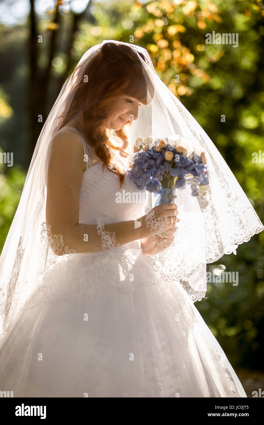 Portrait of bride with long white veil looking at wedding bouquet Stock ...