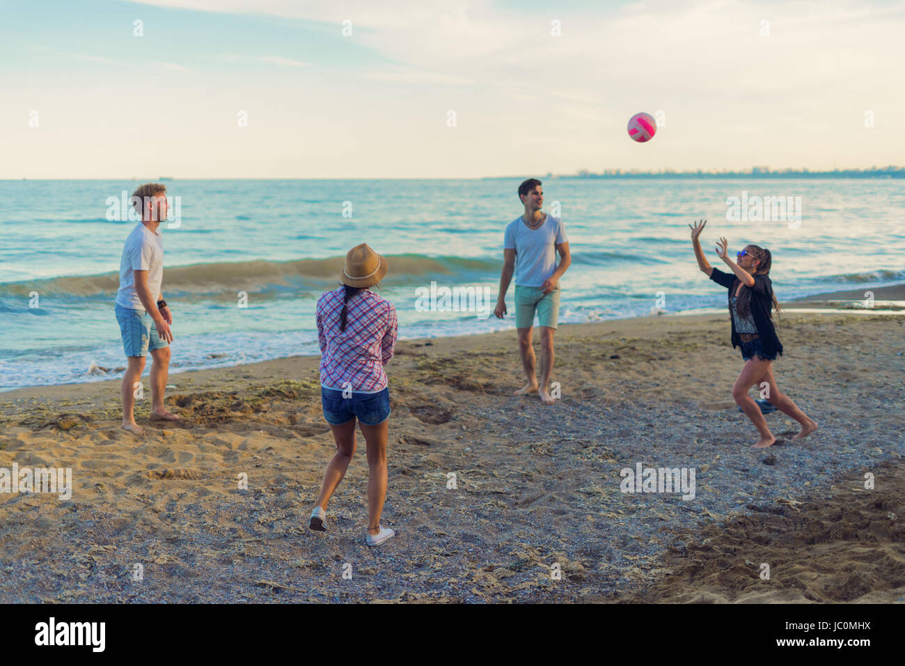 friends playing volleyball on a wild beach during sunset Stock Photo