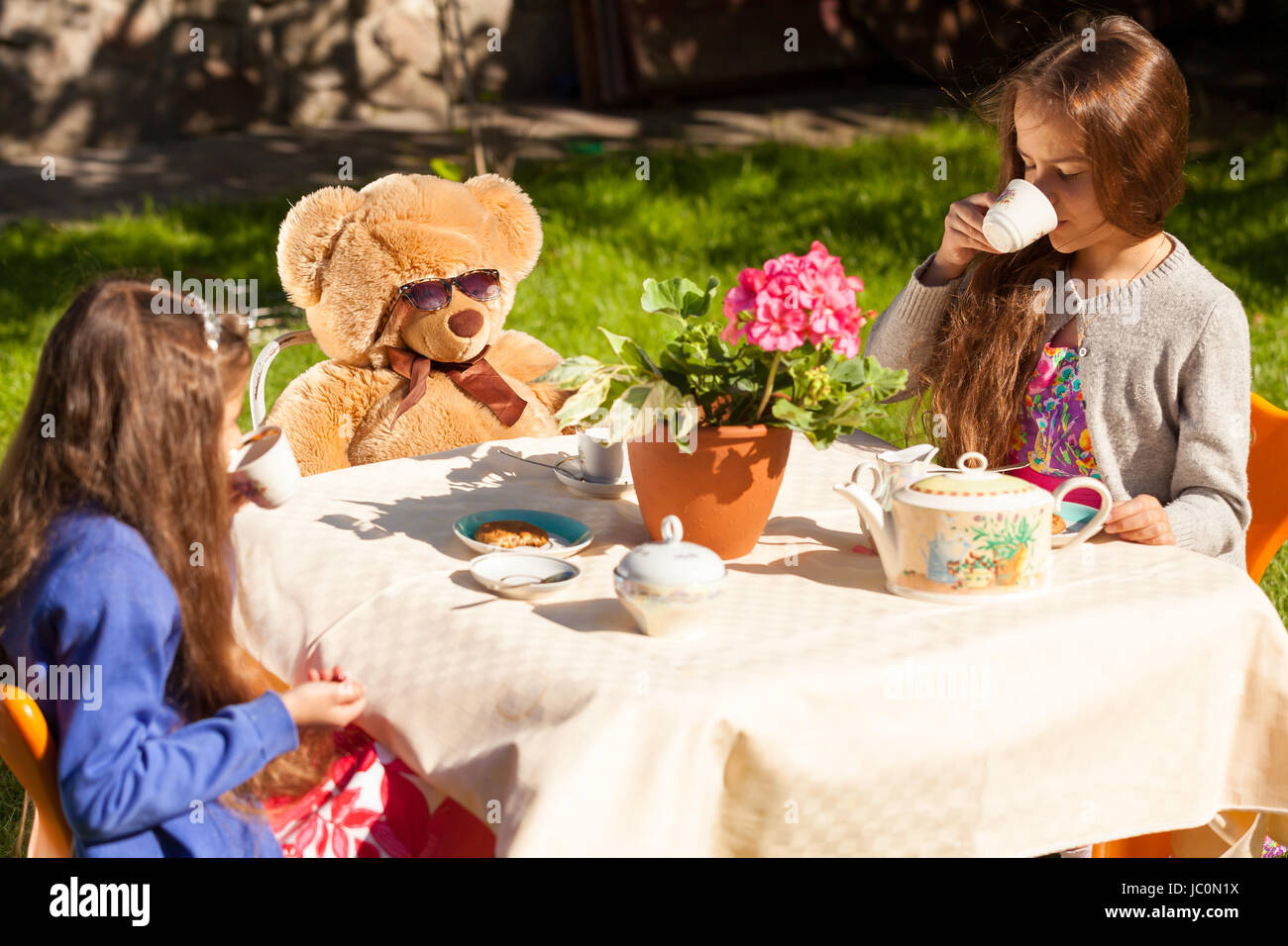 Two little sisters having english breakfast with teddy bear at yard Stock Photo