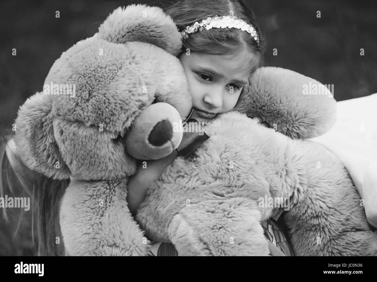 Black and white portrait of small crying girl hugging teddy bear Stock Photo