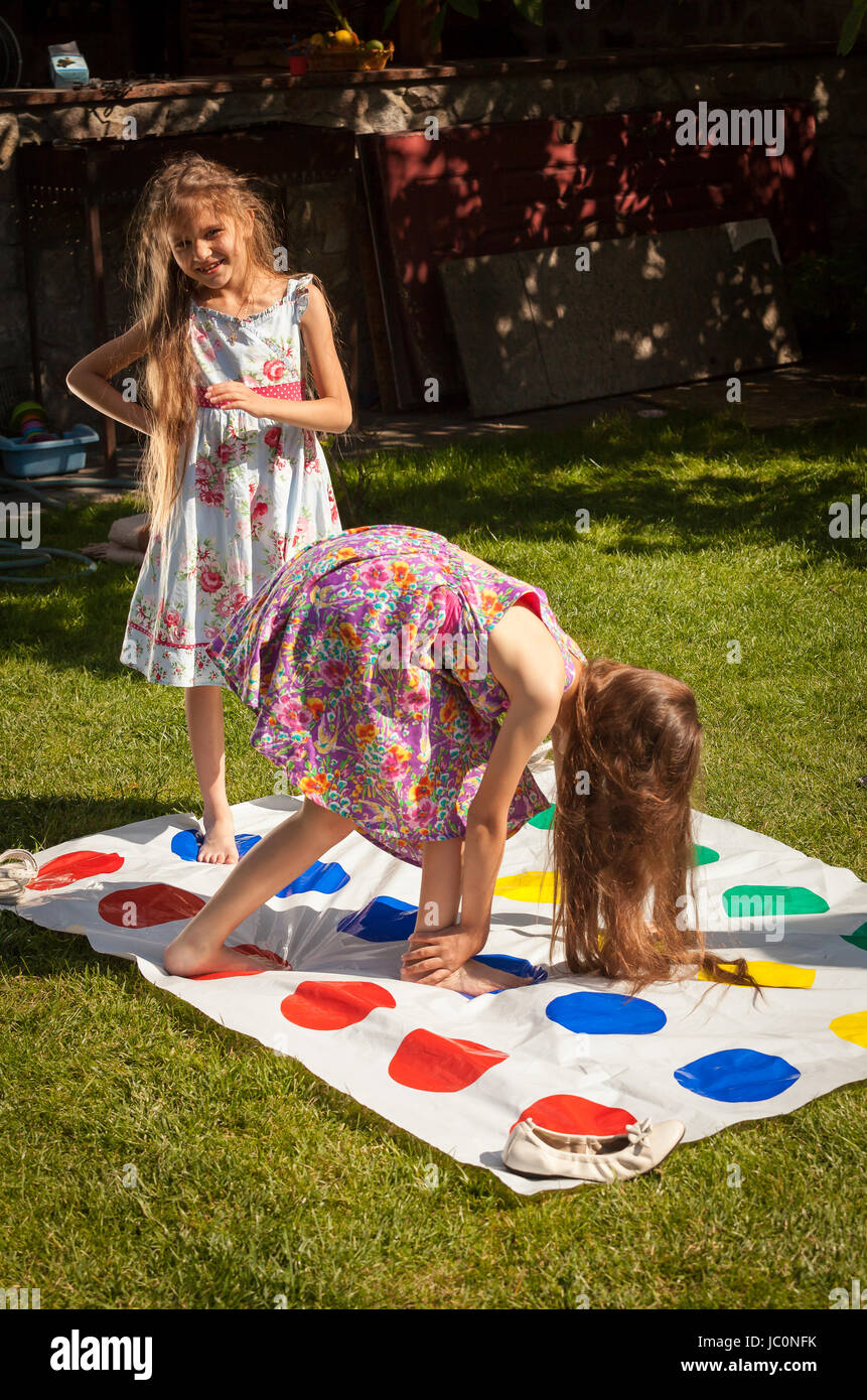 Two little sisters playing twister game at yard on grass Stock Photo