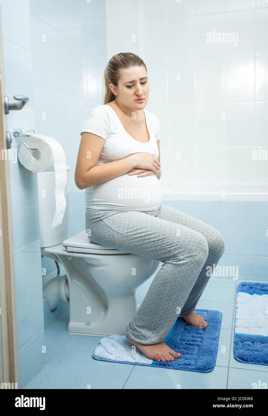 Young sick pregnant woman witting on the toilet Stock Photo
