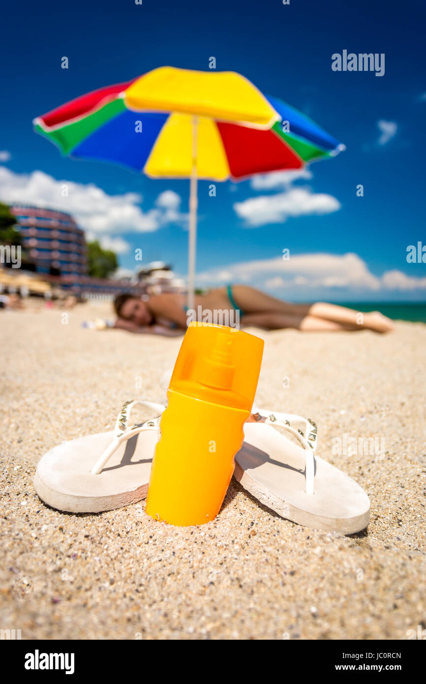 Closeup shot of pair of flip-flops and sunblock lotion lying on sandy beach Stock Photo