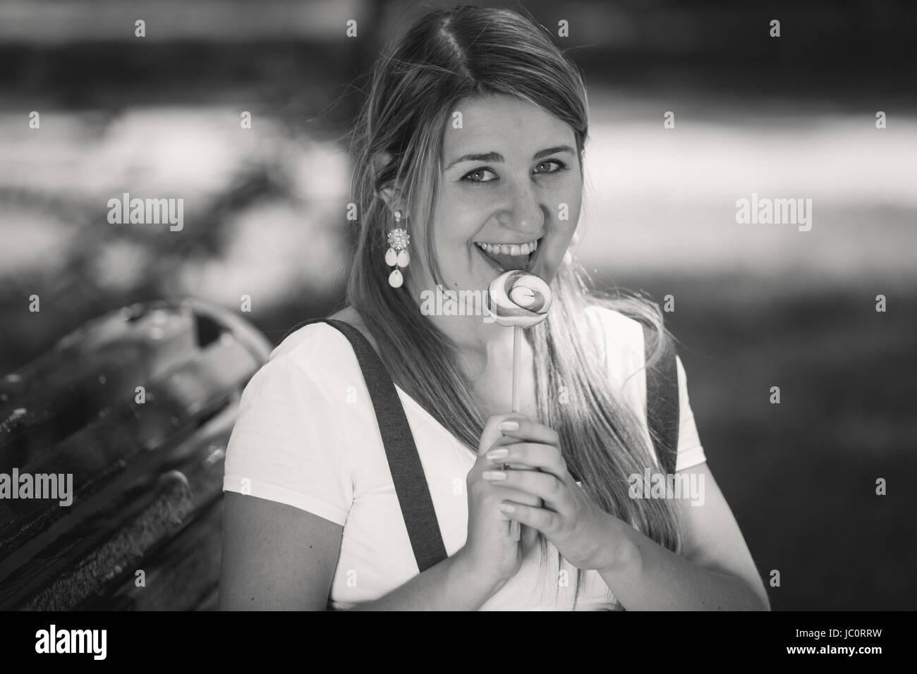 Black and white portrait of cute woman licking lollipop at park Stock Photo