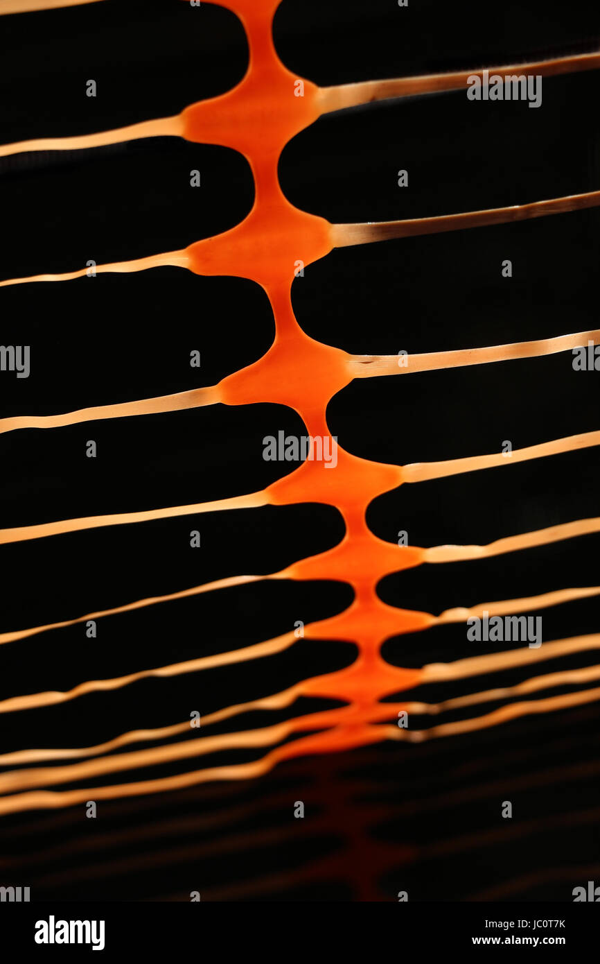 Orange abstract pattern created by section of a flexible plastic construction retaining fence, backlit in the sunlight gives it a black background.... Stock Photo