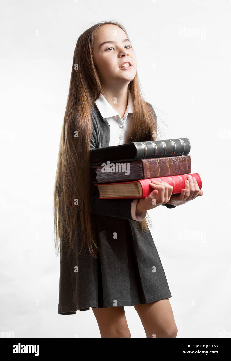 Portrait of schoolgirl carrying heavy stack of books against white ...