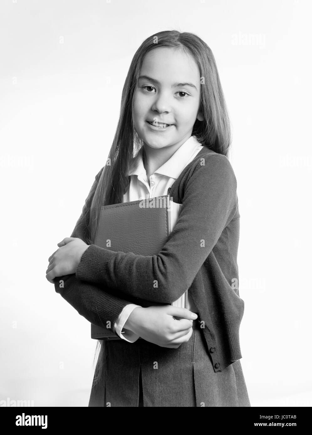 Black and white portrait of smiling schoolgirl posing with book at studio Stock Photo