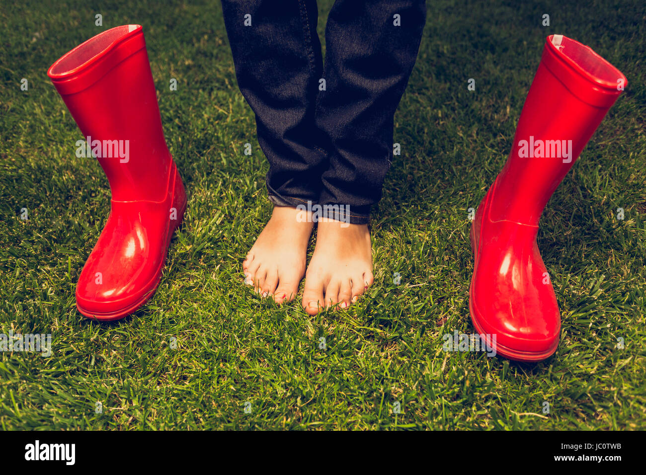 Closeup toned photo of barefoot girl posing with red gumboots on meadow ...