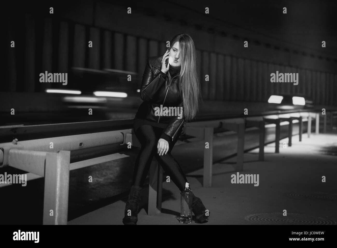 Black and white photo of young stylish woman talking by phone at night highway Stock Photo