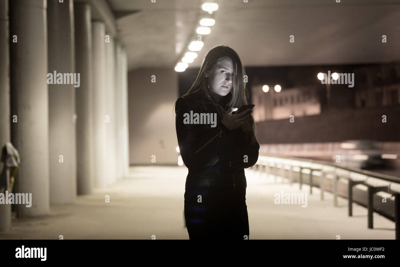 Toned portrait of lonely woman using mobile phone at night on street Stock Photo