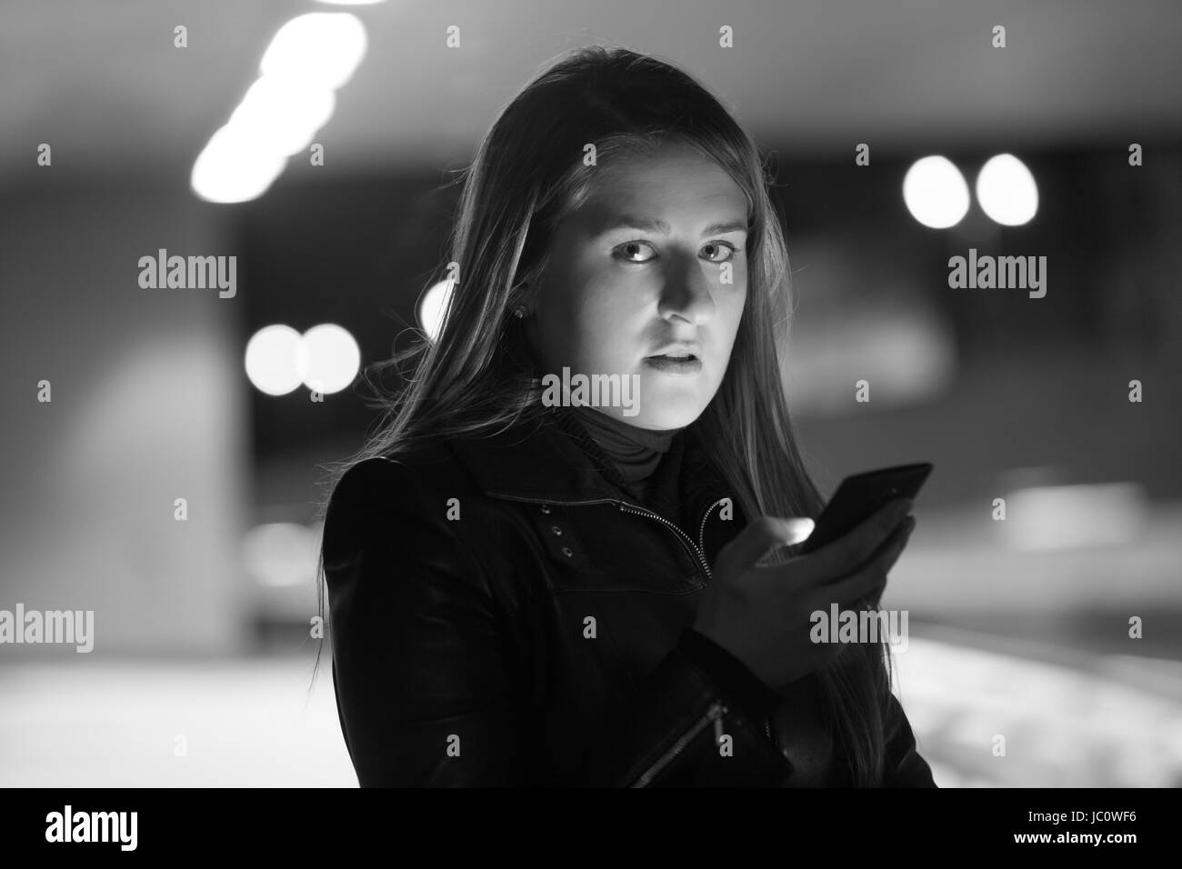 Closeup black and white portrait of lonely woman posing on dark street with telephone Stock Photo