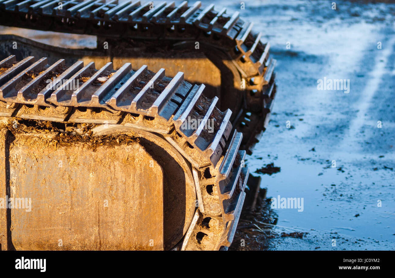 Part of industrial caterpillar tracks in afternoon sun on muddy ground. Stock Photo