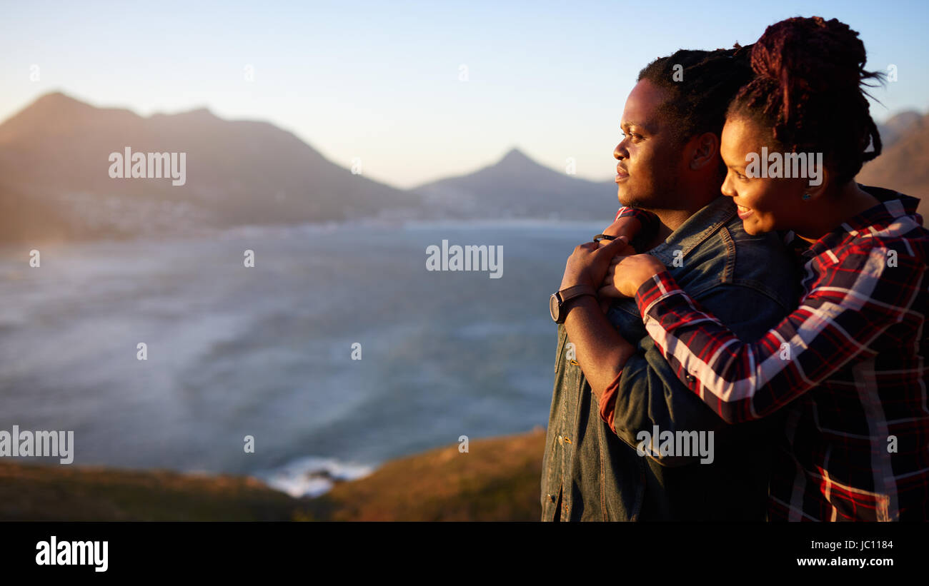 Interracial couple looking at the sunset ocean and mountain view Stock Photo