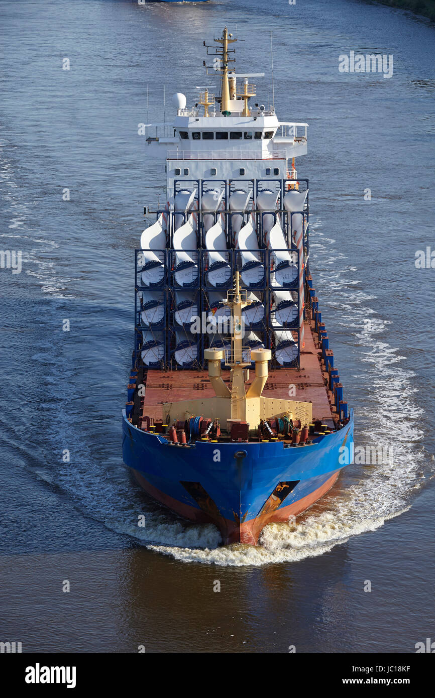 A cargo vessel loaded with rotor blades for wind turbines at the Kiel Canal near Beldorf (Schleswig-Holstein, Germany) taken at daylight. All numbers and words on containers and ship are retouched in this image version. Stock Photo