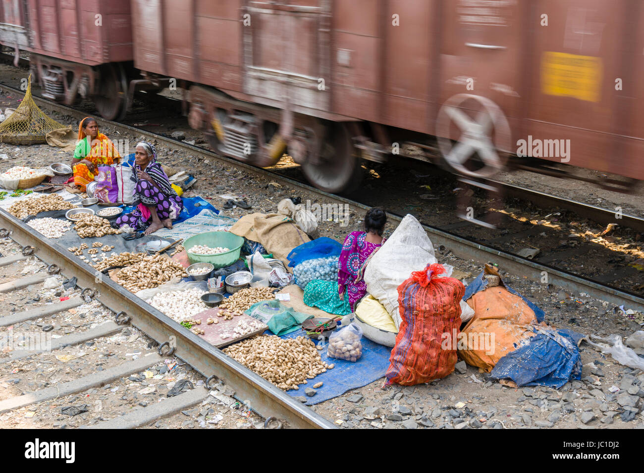 Women are selling vegetables and spices between the railroad tracks at Park Circus Railway Station, a train is passing through Stock Photo