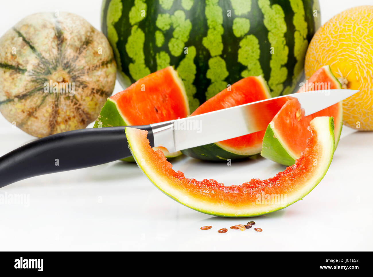 Messer steckt in Melone vor verschiedenen Melonen vor weißem Hintergrund Stock Photo