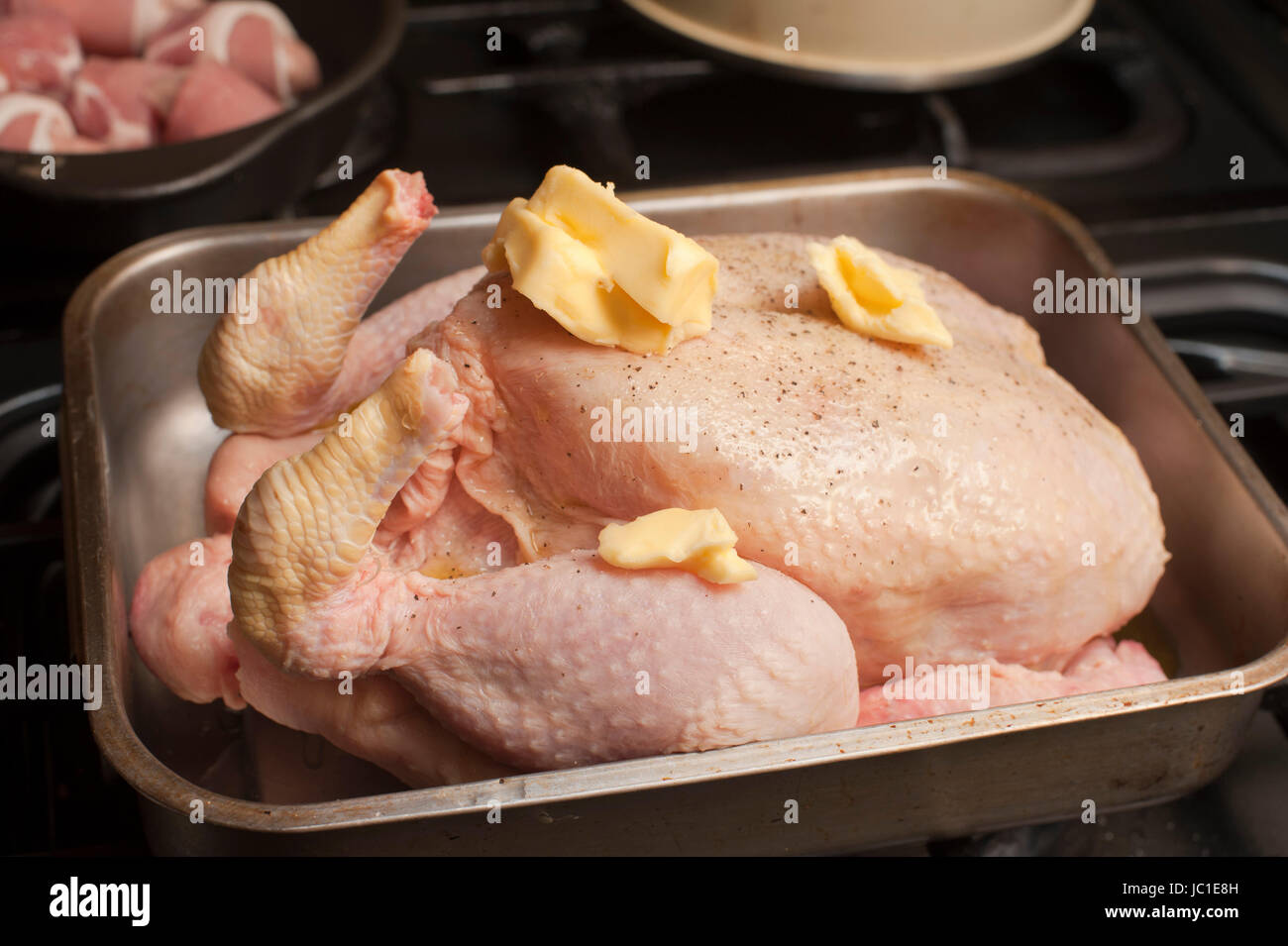 Uncooked seasoned turkey topped with dollops of butter in a roasting pan or oven dish waiting to