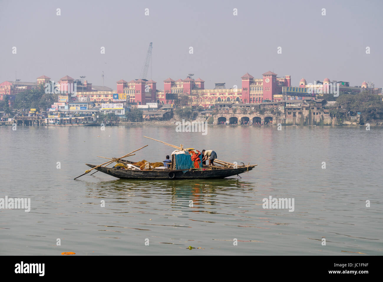 A fishermans boat is crossing the Hoogli River, Howrah Railway Station in the distance Stock Photo